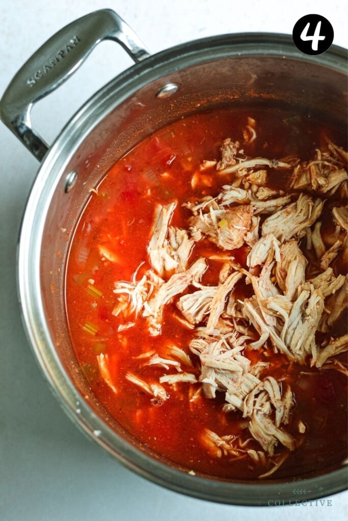 shredded chicken added to red soup in a large pot.