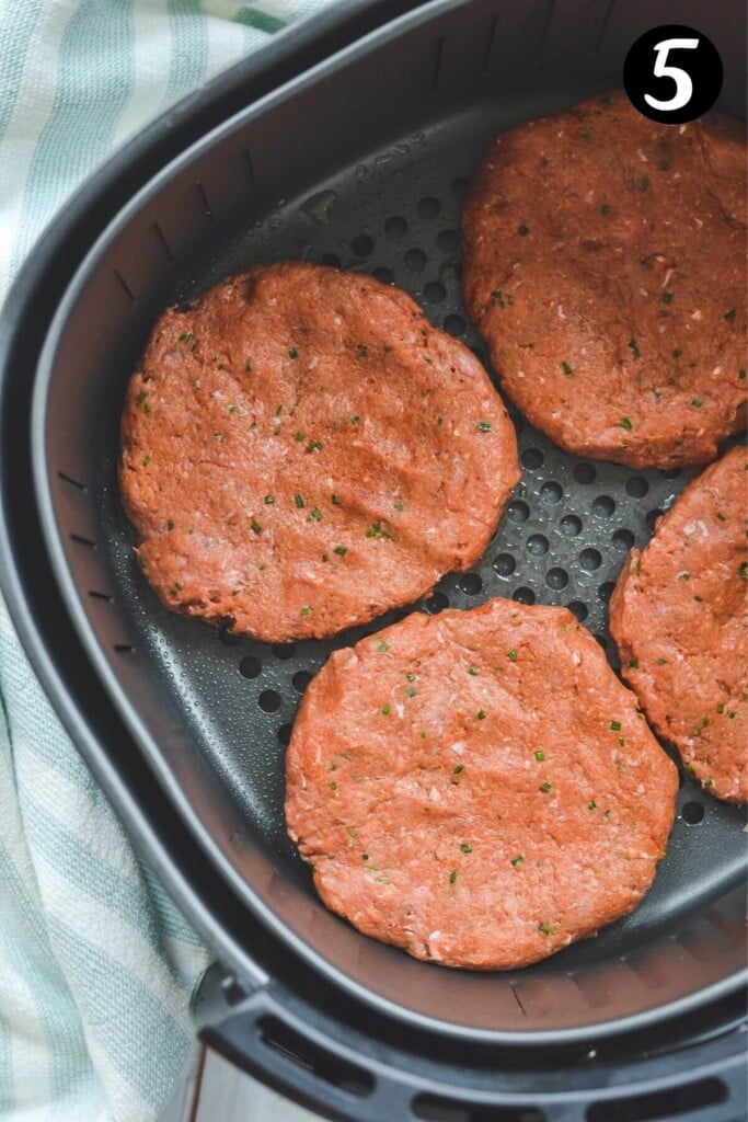 raw burger patties arranged in an air fryer basket.