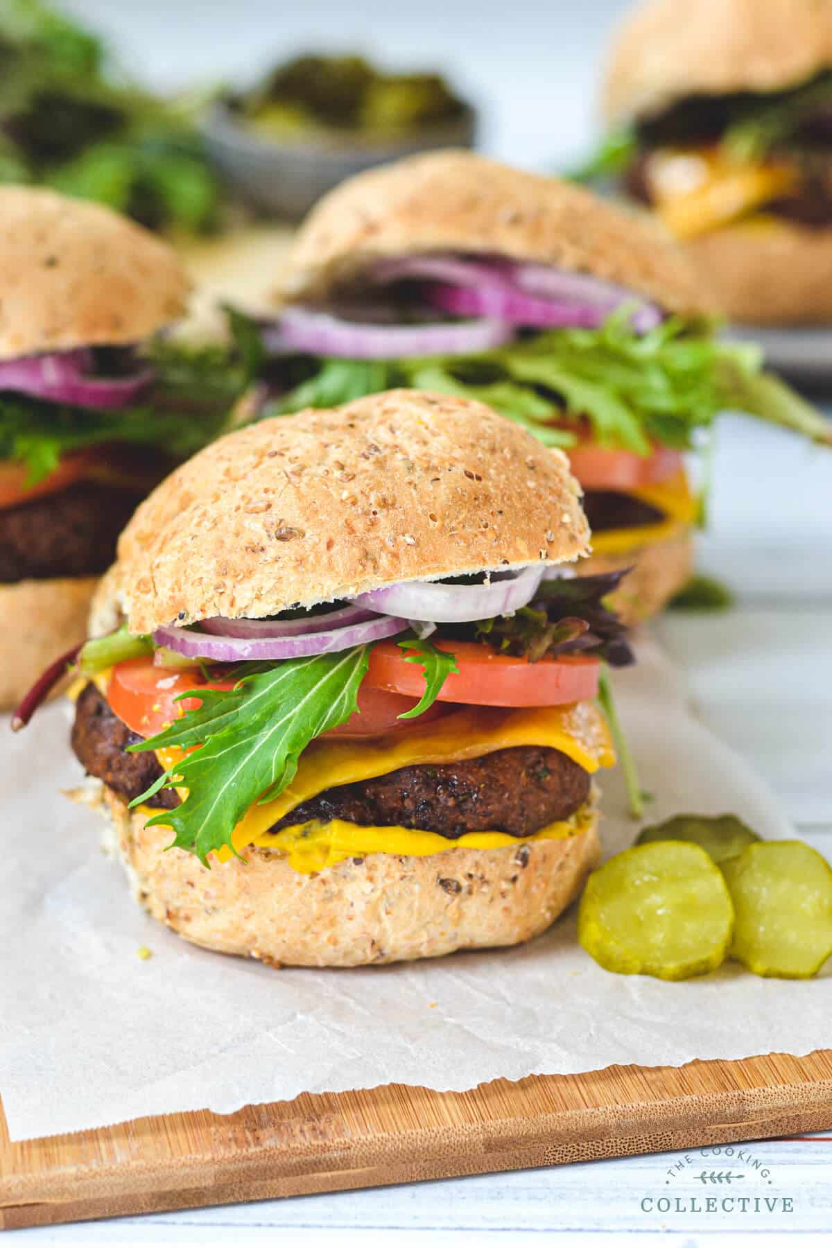 Finished burgers on a wooden board with sliced pickles.