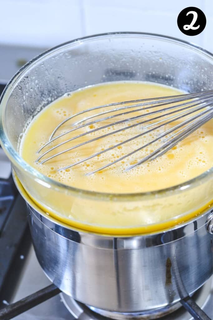 lemon curd mixture in a glass bowl over a saucepan