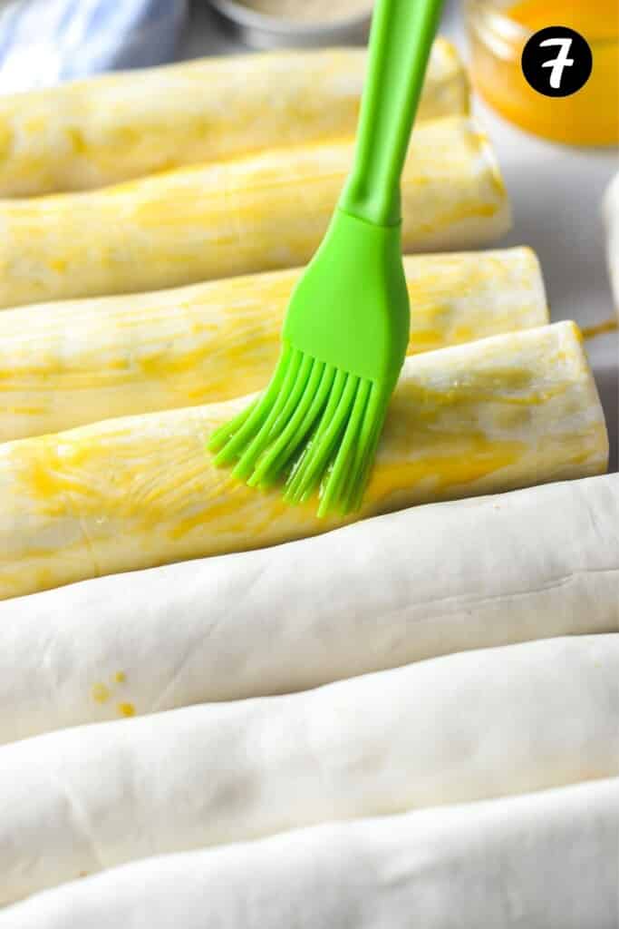 a pastry brush spreading egg mixture over puff pastry rolls