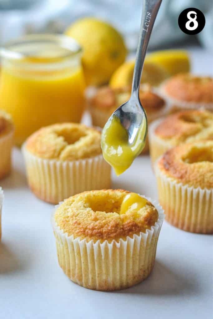 a spoon dropping lemon curd into hollowed out cupcakes