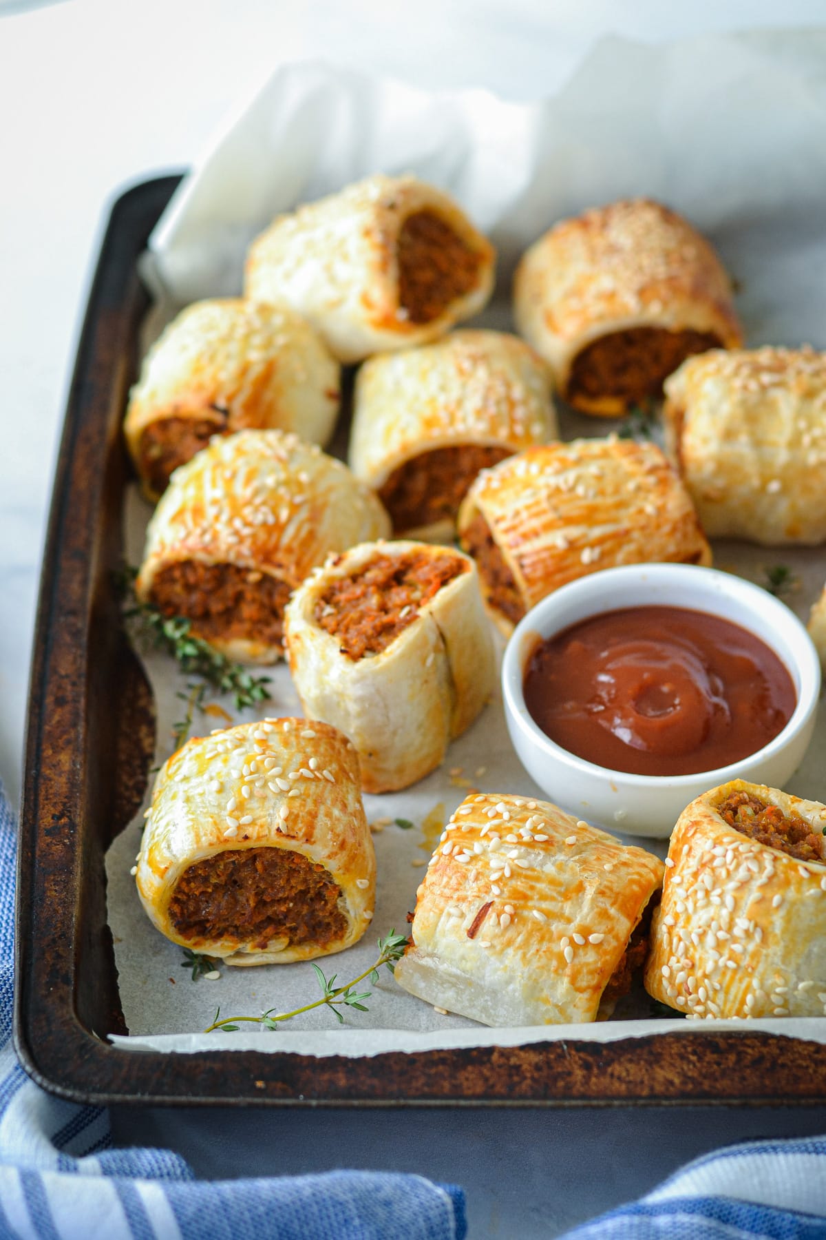 sausage rolls spread out on a baking tray with a dish of tomato sauce