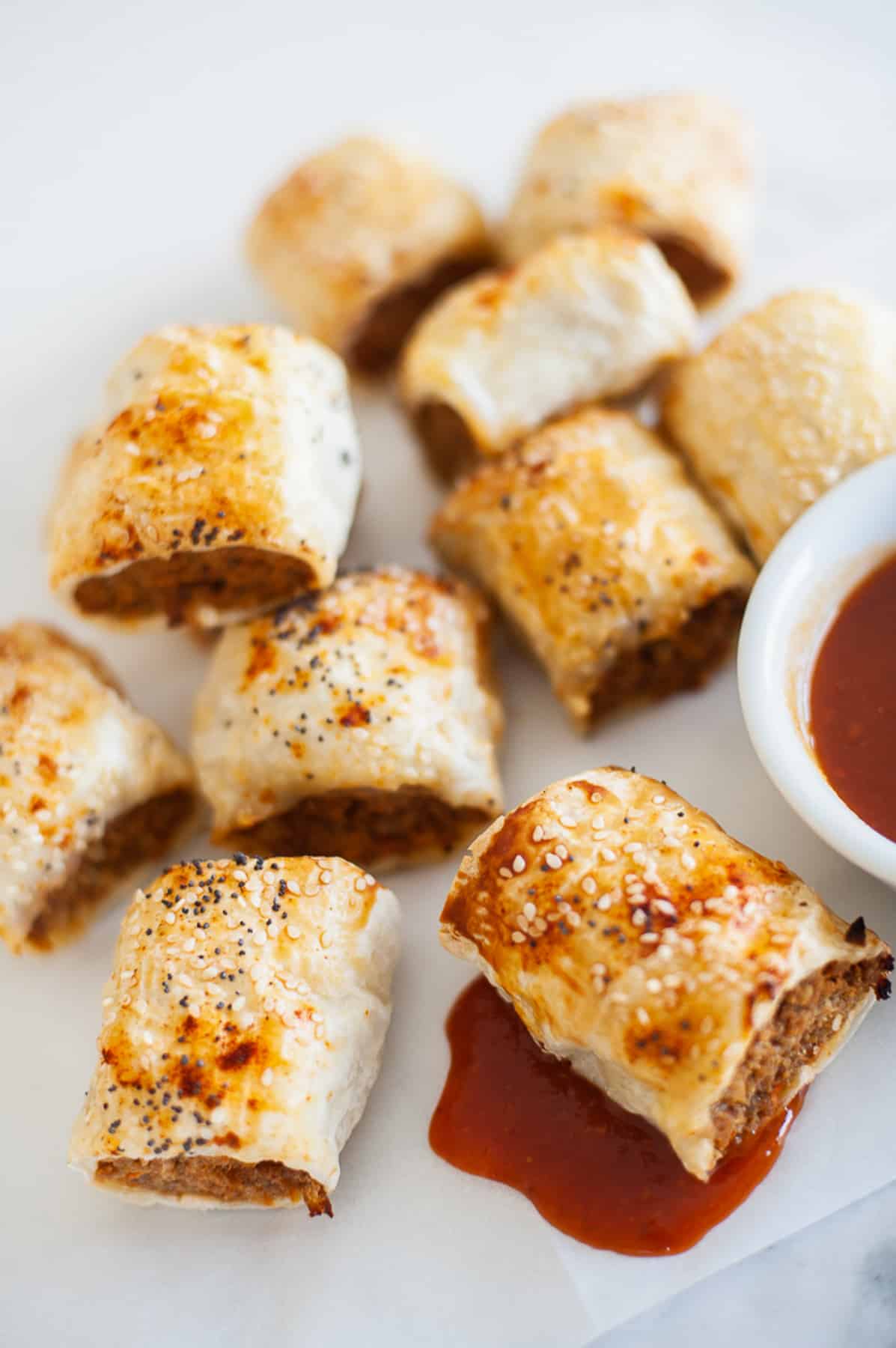 mini sausage rolls on a white board with tomato sauce