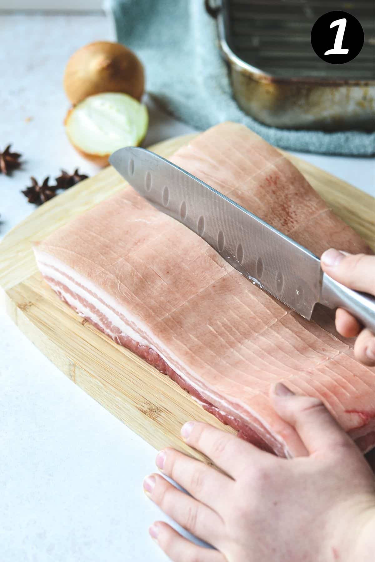 a knife scoring pork belly skin on a white bench