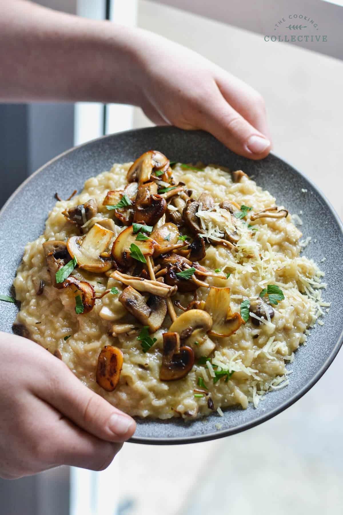 hands holding a grey plate with mushroom risotto