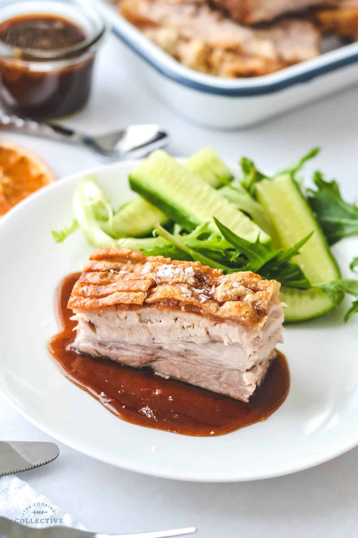 a slice of pork belly with sauce and green salad on a white plate