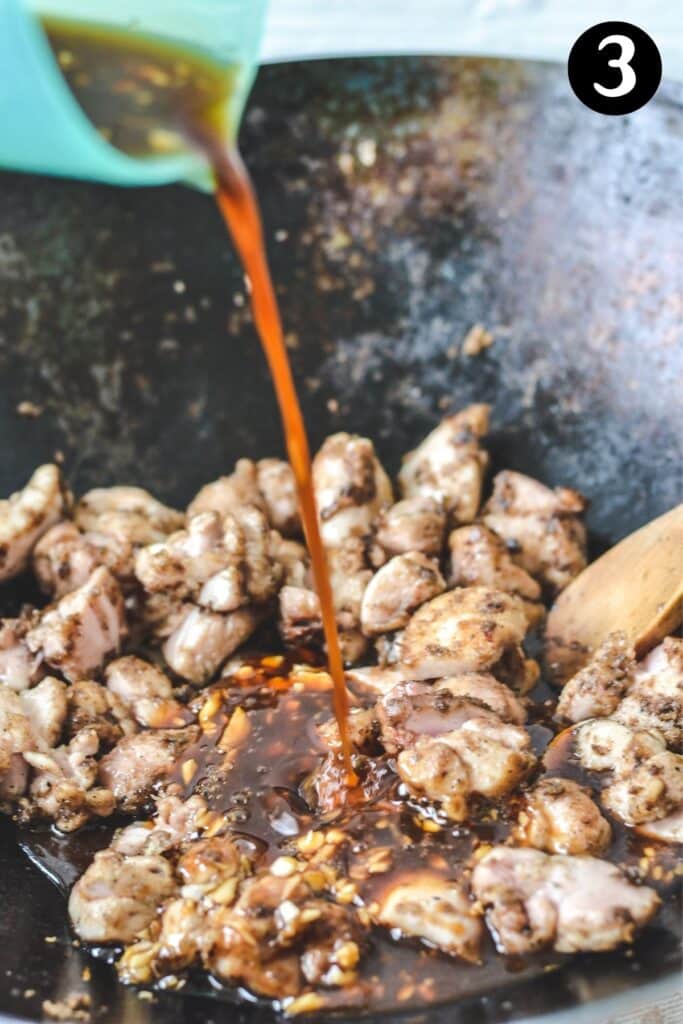 oyster sauce mixture being poured over chicken in a wok