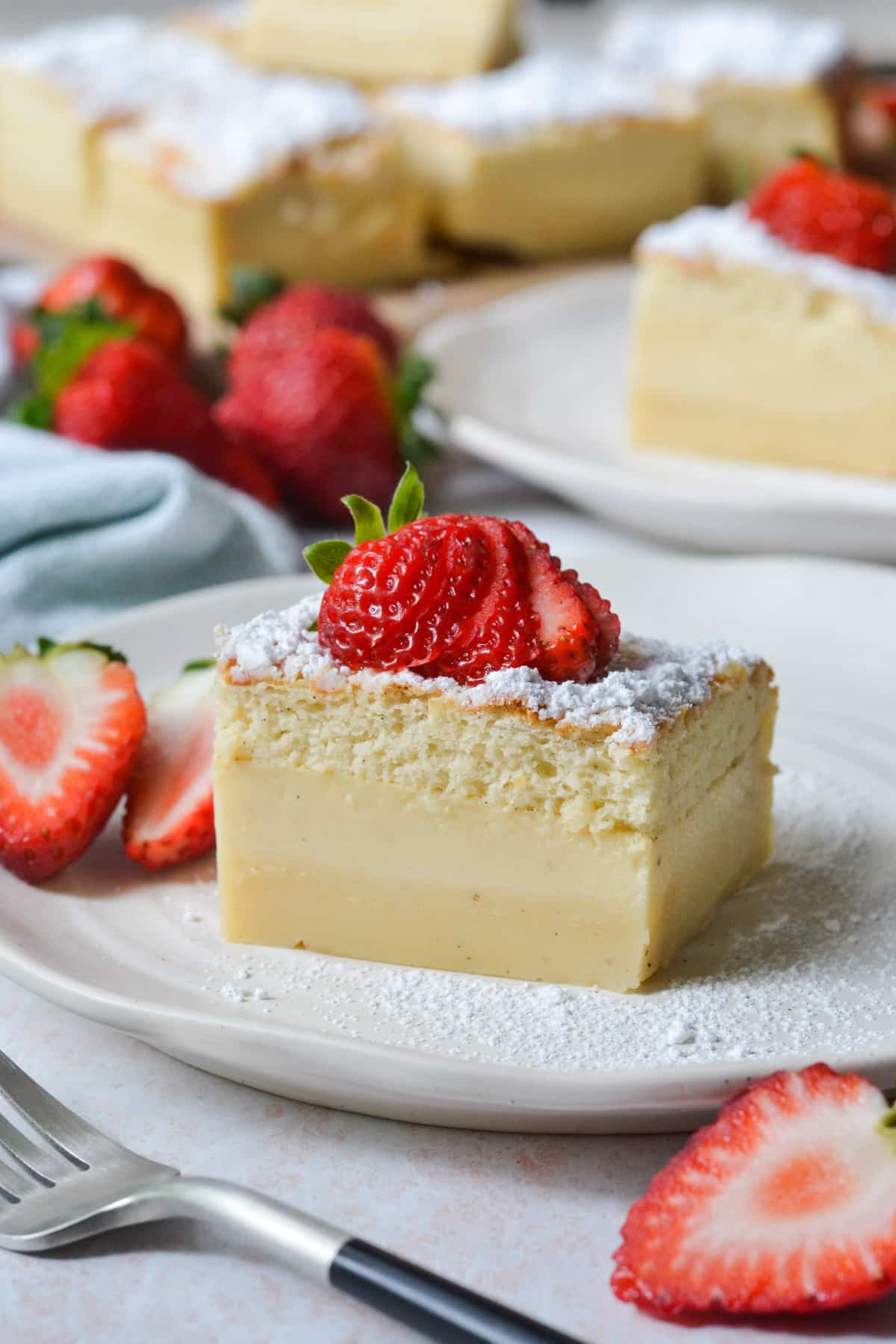 a slice of custard cake on a plate, surrounded by strawberries