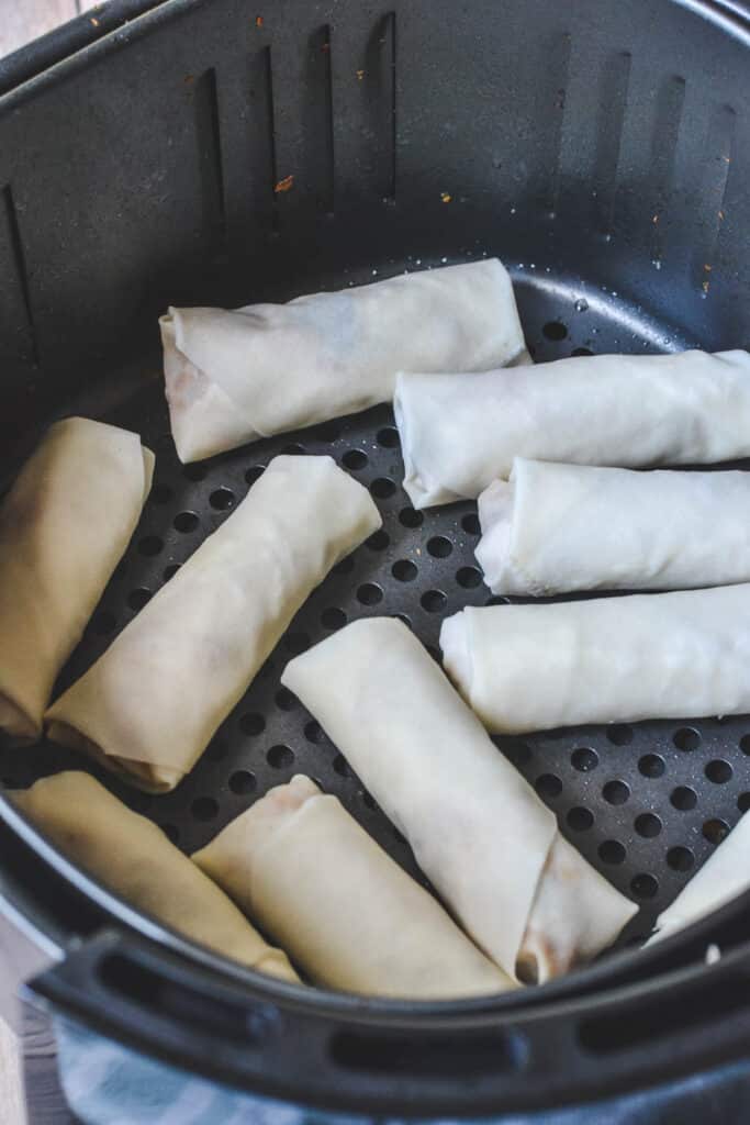 uncooked spring rolls in an air fryer basket