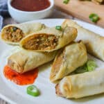 close up of spring rolls on a white plate with spring onion and sauce