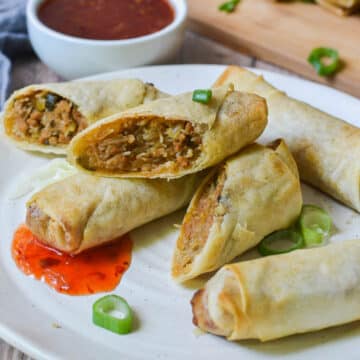 close up of spring rolls on a white plate with spring onion and sauce