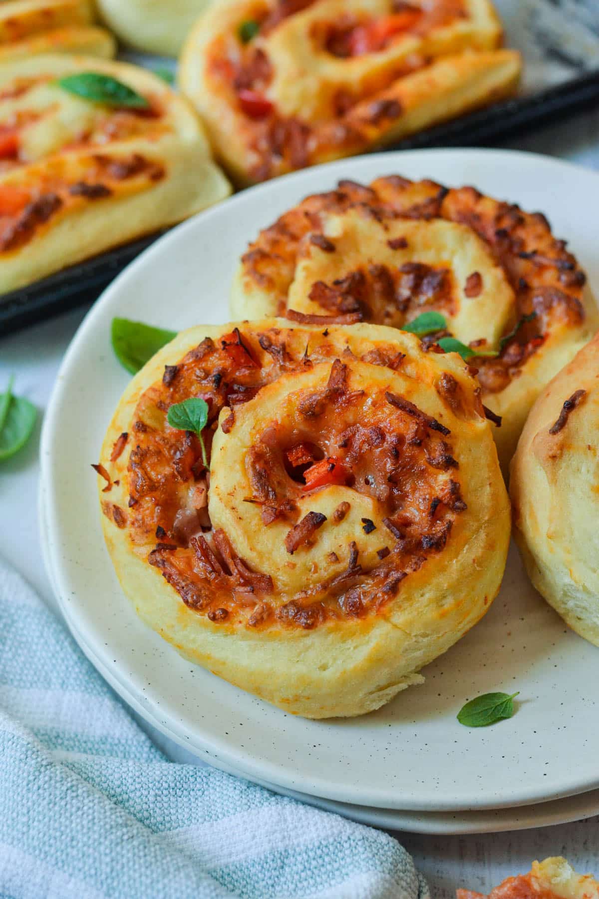 close up of finished pizza scrolls on a white plate topped with basil leaves