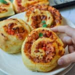 a hand holding a pizza scroll over a white plate