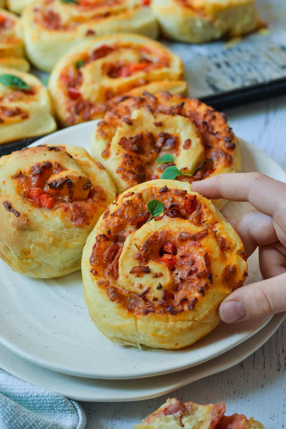 a hand holding a pizza scroll over a white plate