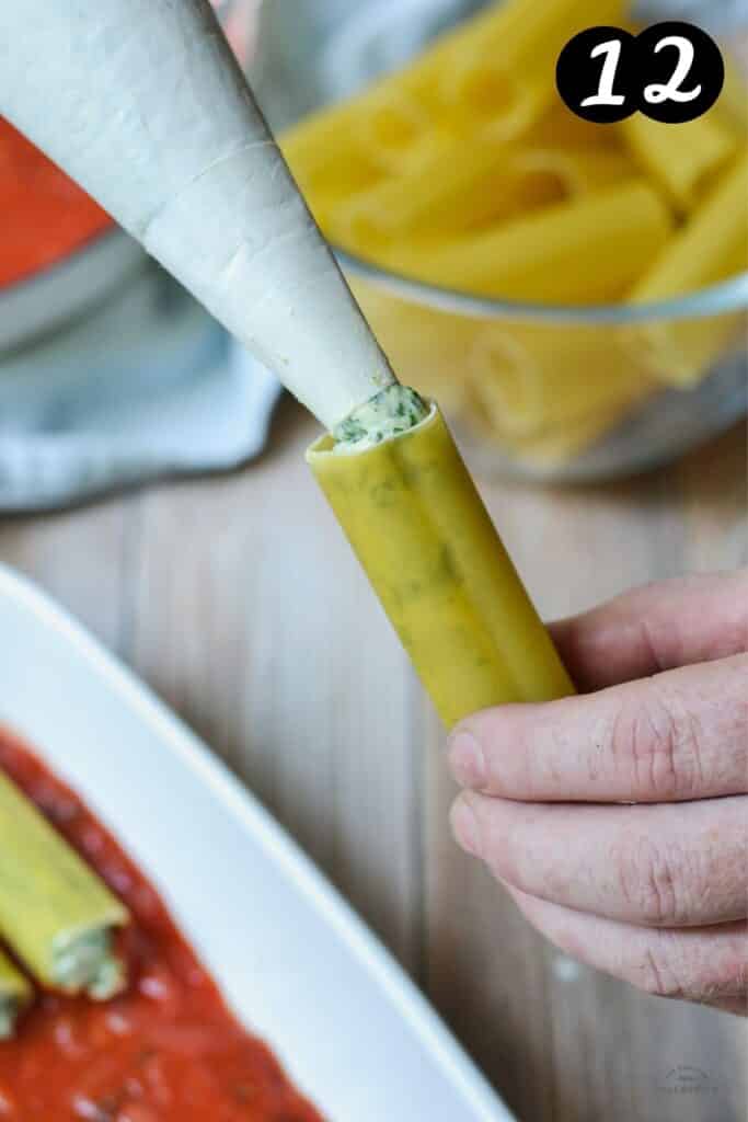 a hand filling a cannelloni pasta tube using a piping bag