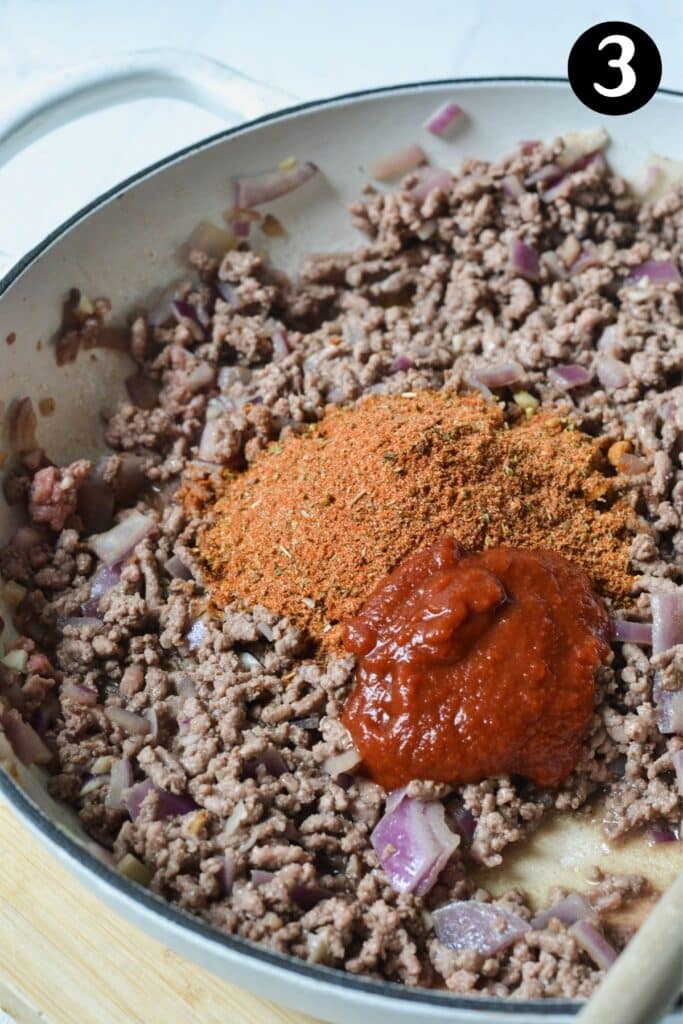 browned beef in a white pan with taco seasoning and tomato paste