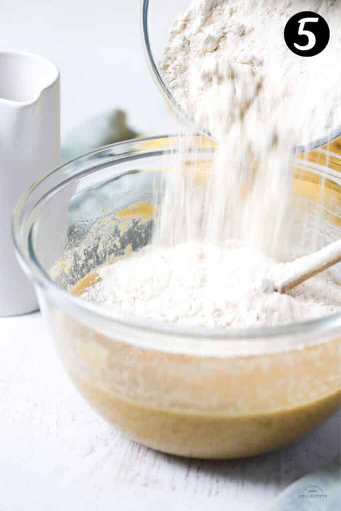 flour being added to banana cake batter in a bowl