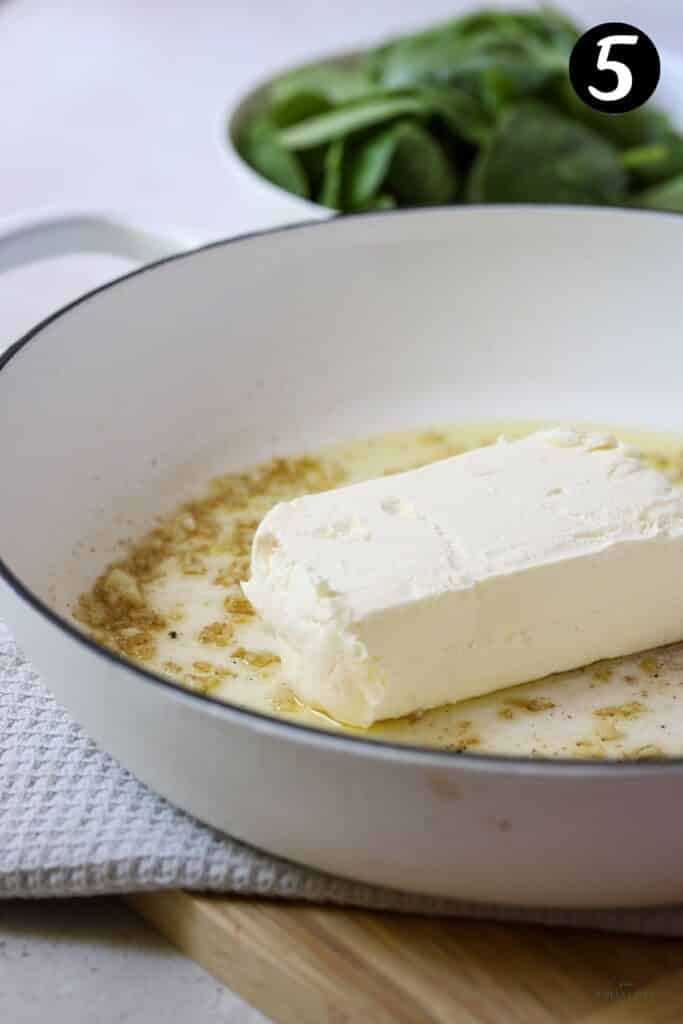 a block of cream cheese in a white pan with garlic and oil
