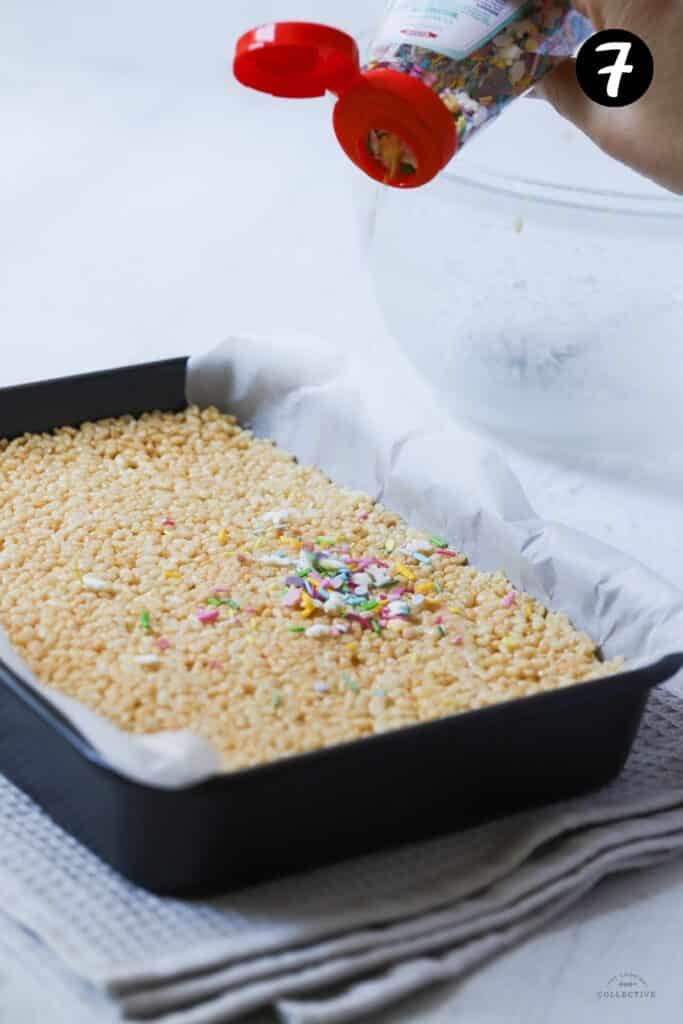 sprinkles being poured over rice bubble slice in a tin