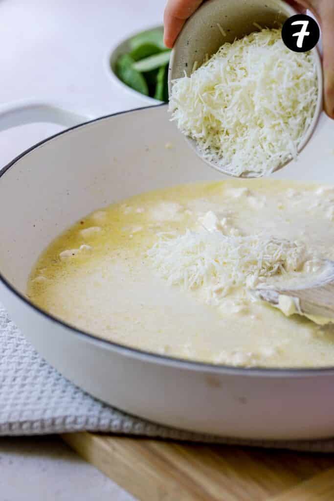 grated cheese being added to cream cheese pasta sauce in a pan