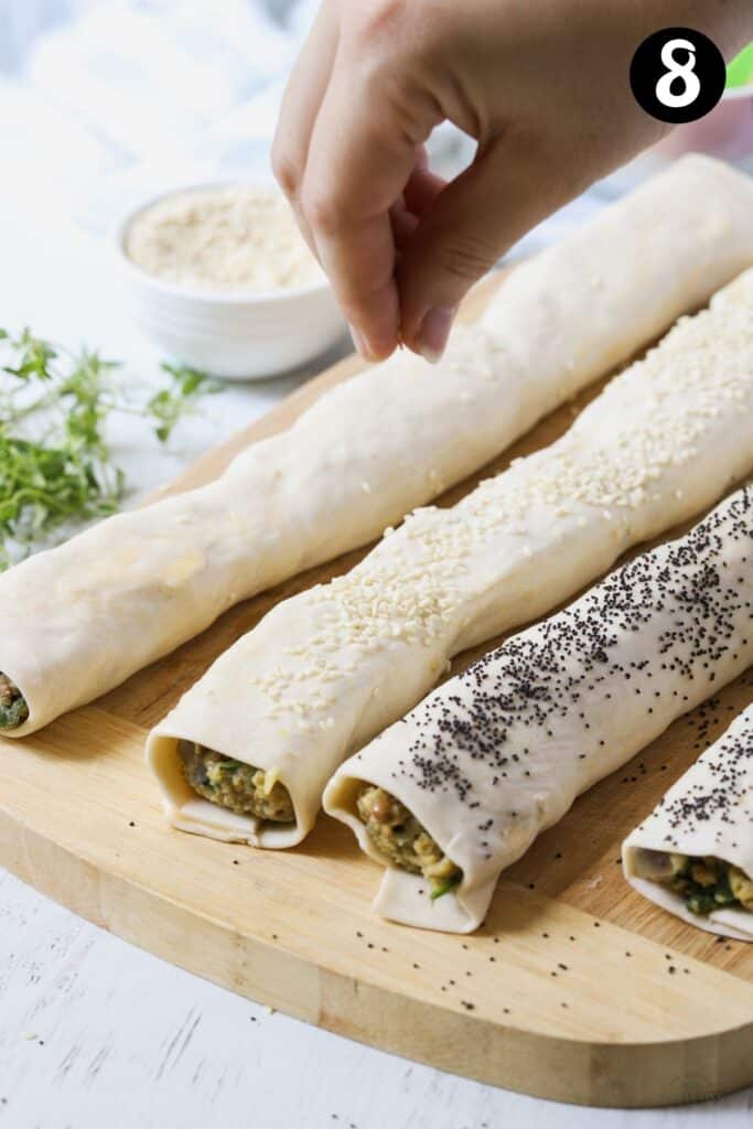 sausage rolls being topped with sesame and poppy seeds