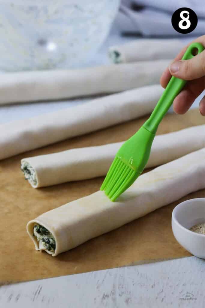 a pastry brush brushing egg over a spinach and ricotta roll