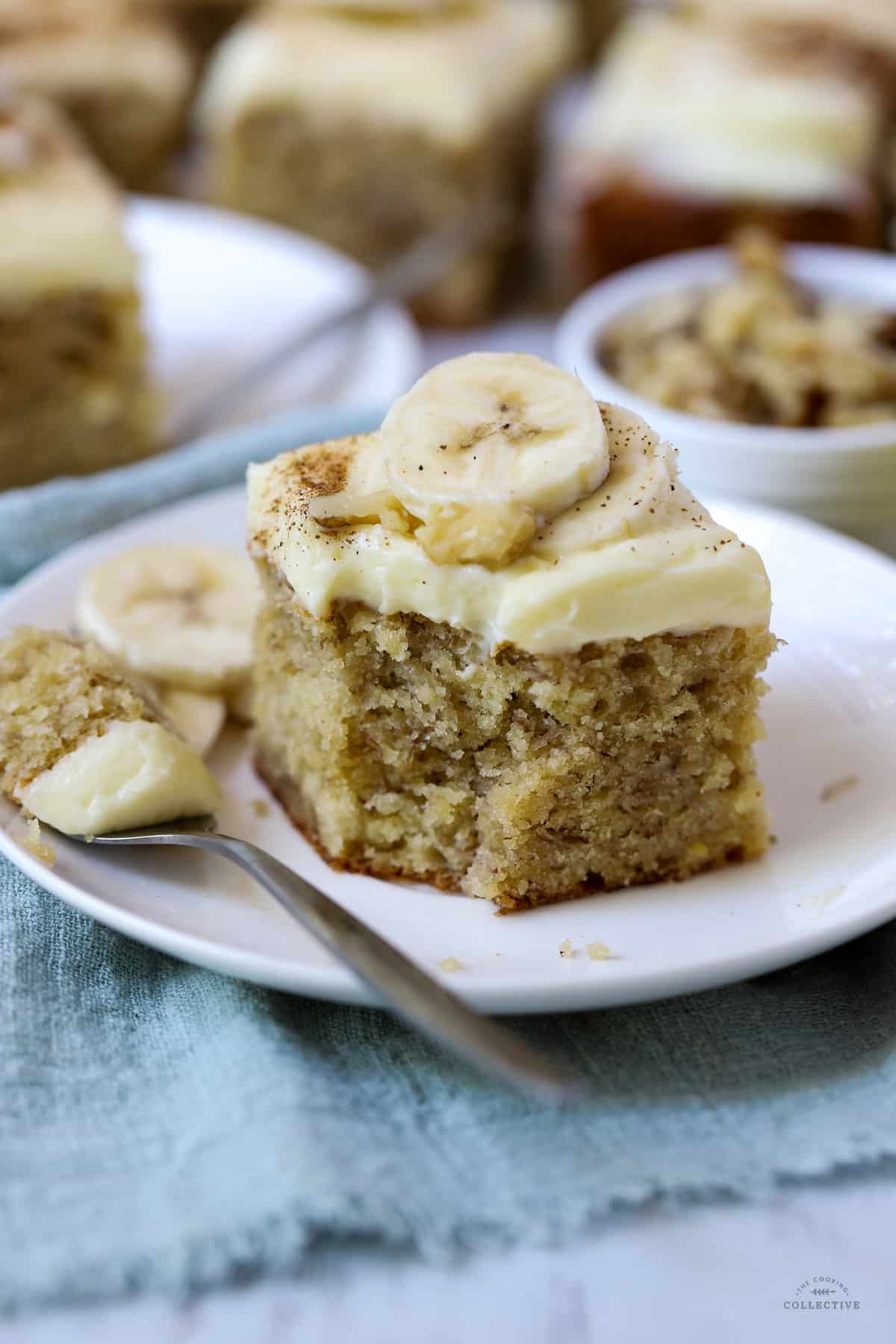 a piece of banana cake topped with cream cheese frosting and banana slices on a white plate