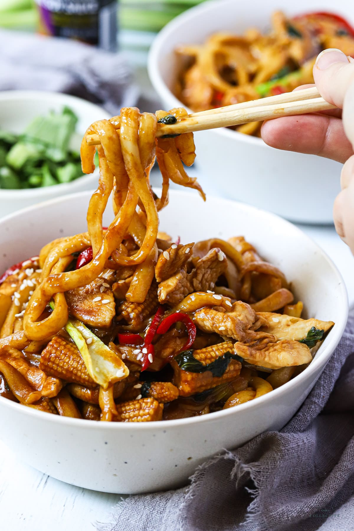 stir fried noodles in a white bowl held with chopsticks