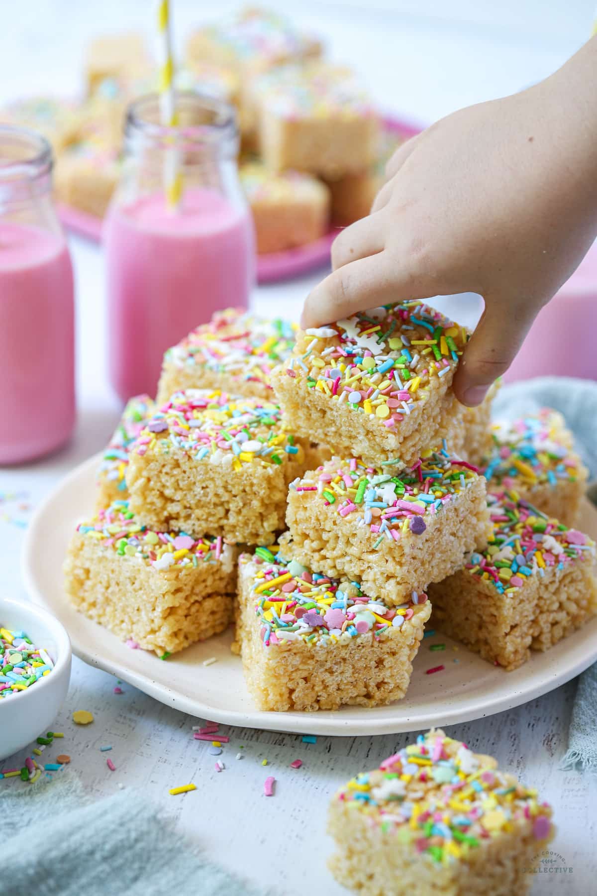 a hand holding a piece of rice bubble slice topped with sprinkles