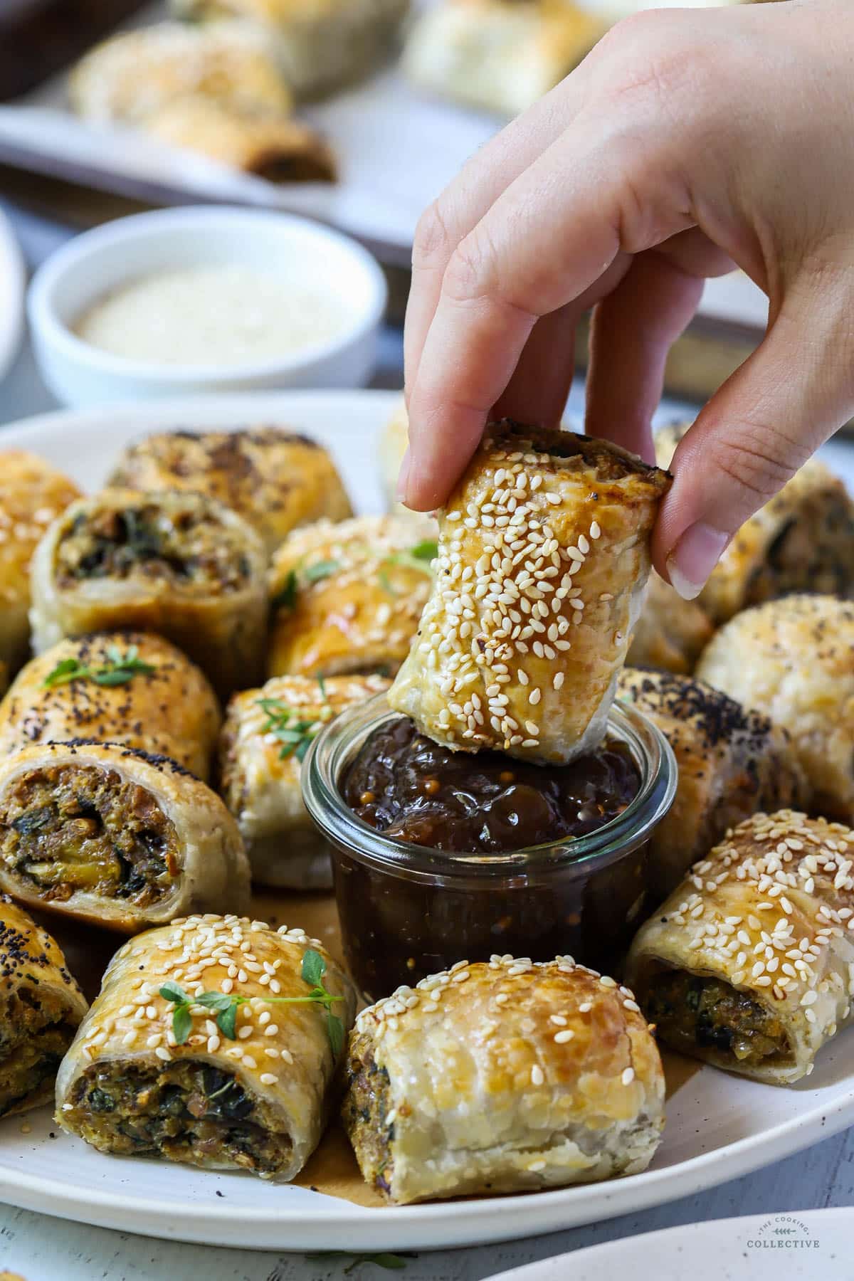 a hand holding a sausage roll and dipping it in sauce