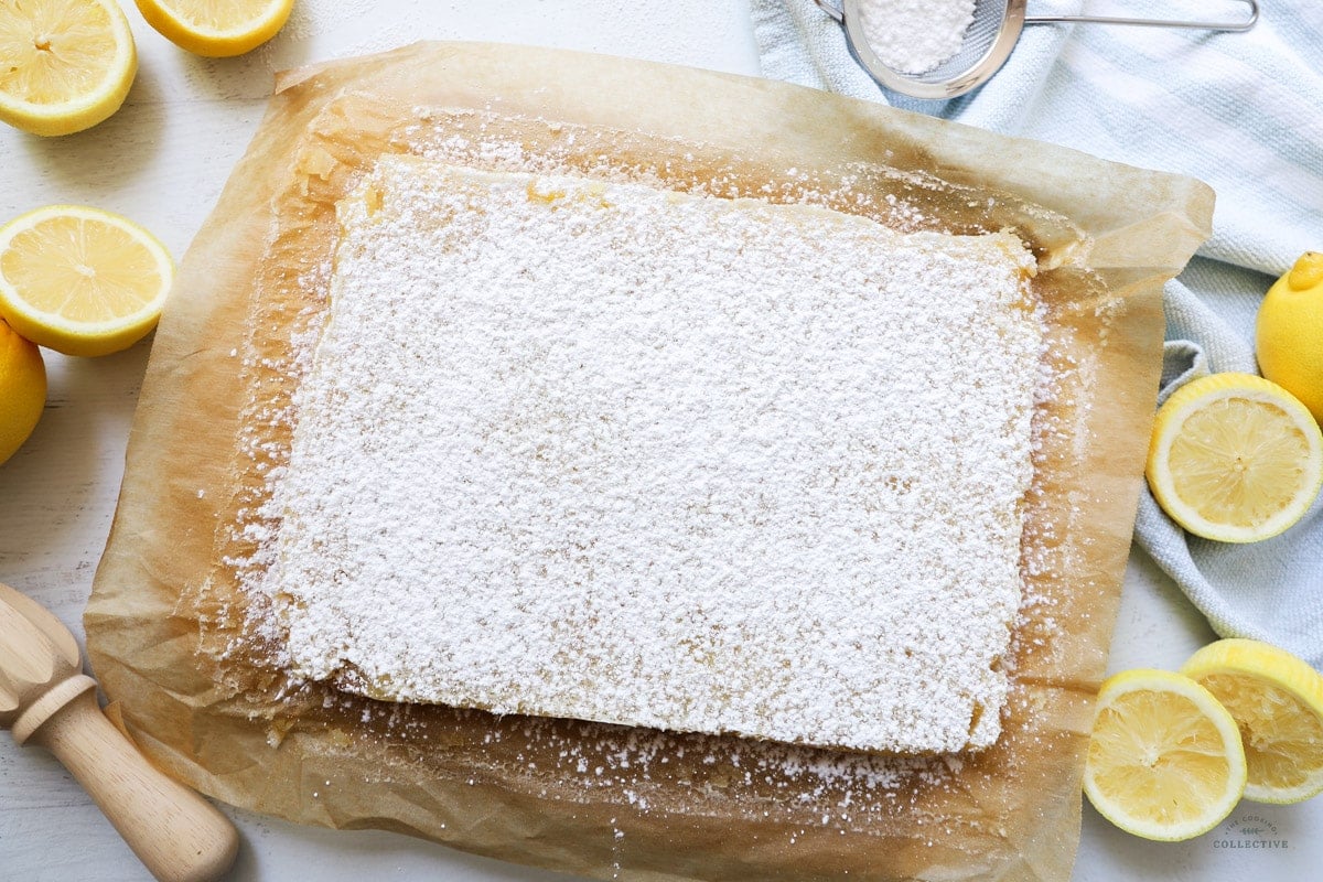 lemon curd slice topping with icing sugar on brown baking paper with lemon halves