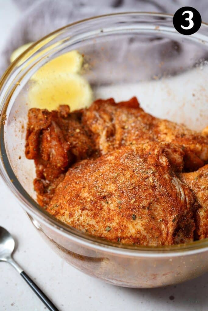 chicken thighs coated in a dry spice rub in a glass bowl