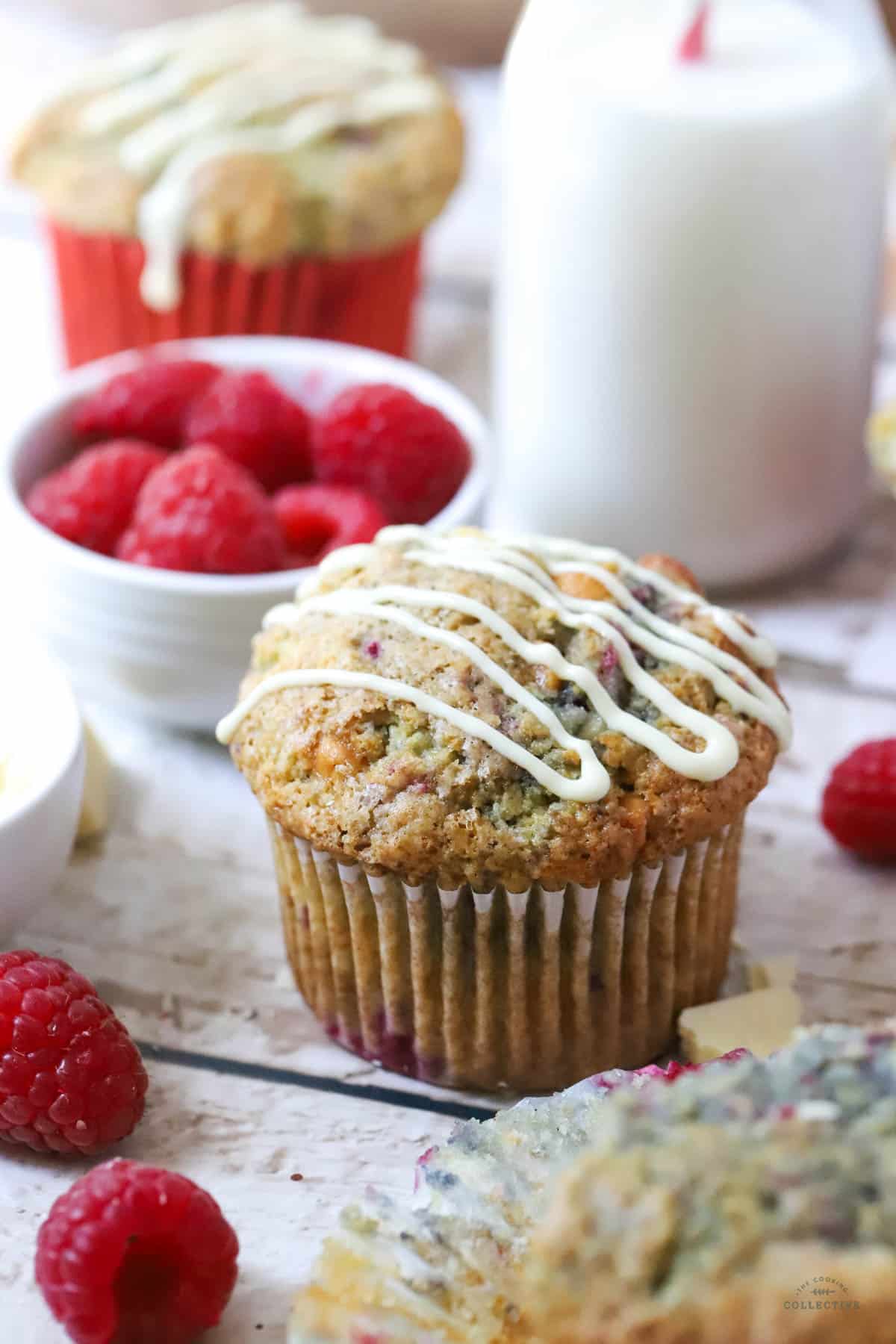 a finished muffin on a wooden table with white chocolate and a bowl of raspberries