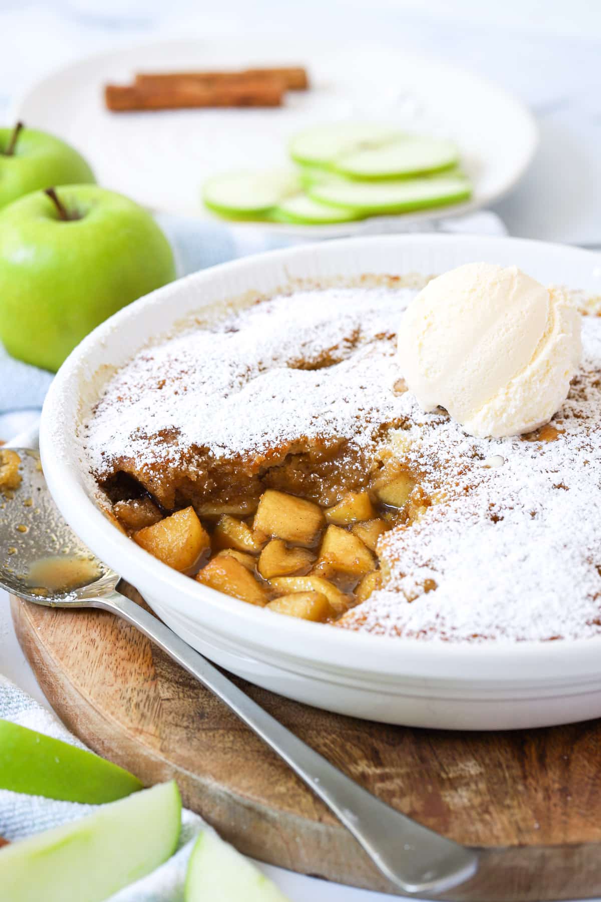 a sponge pudding in a white dish with cooked apples and ice cream