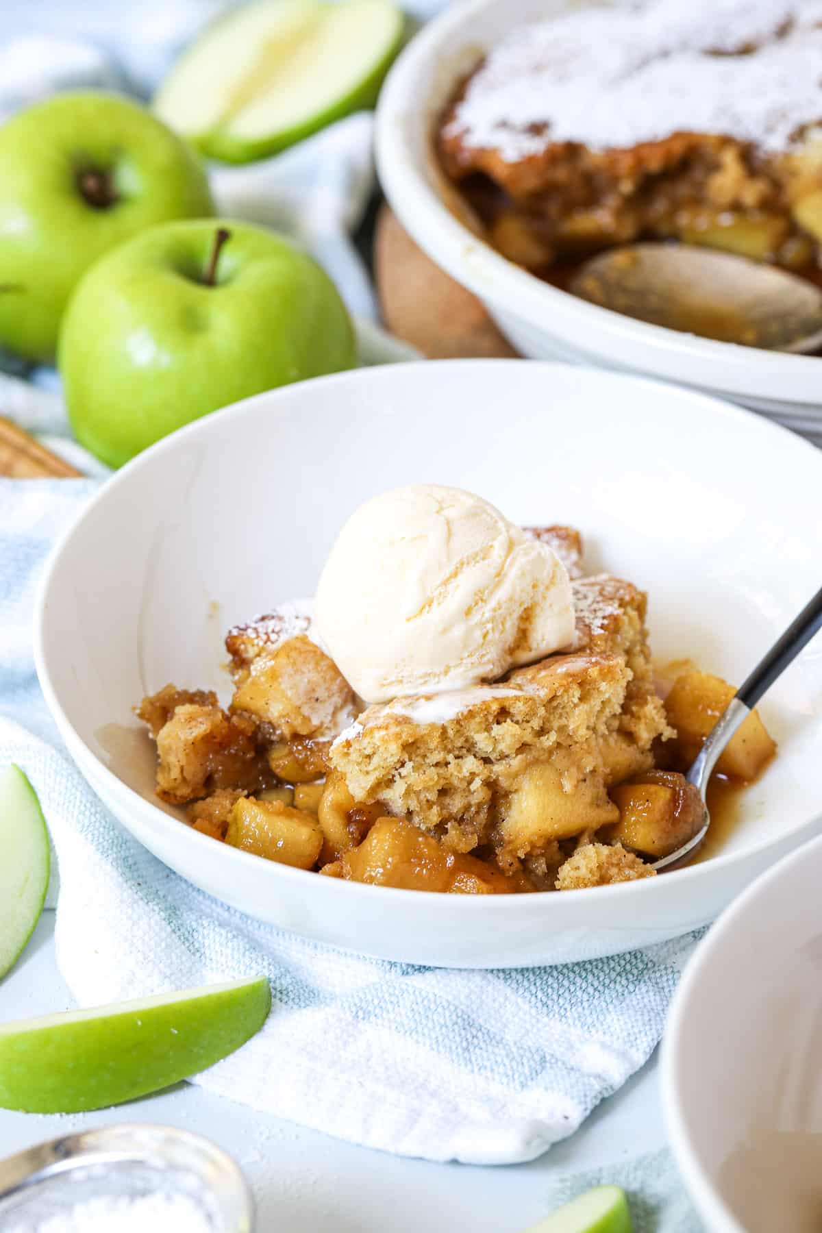 apple sponge pudding in a white bowl with a scoop of ice cream