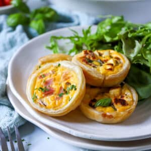 mini puff pastry quiches on a white plate with salad