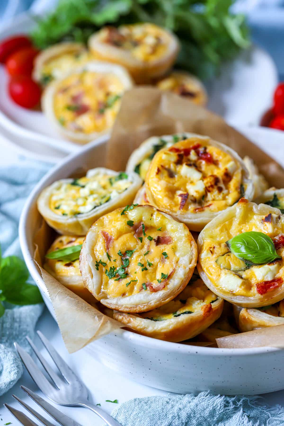 a bowl of mini quiches on a table with plates and forks