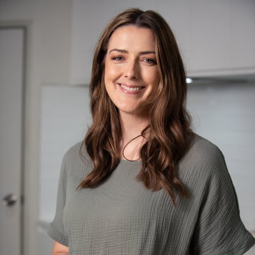 a woman in a green top smiling in a kitchen