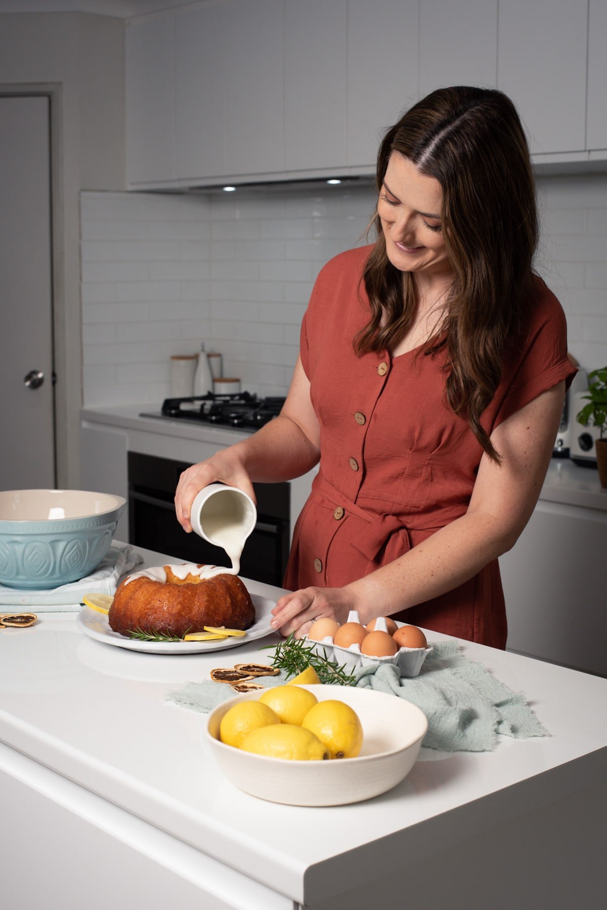 a woman in a kitchen pouring icing over a cake