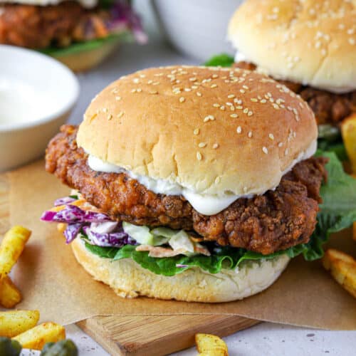 a finished crispy chicken burger on a wooden board with salad and coleslaw