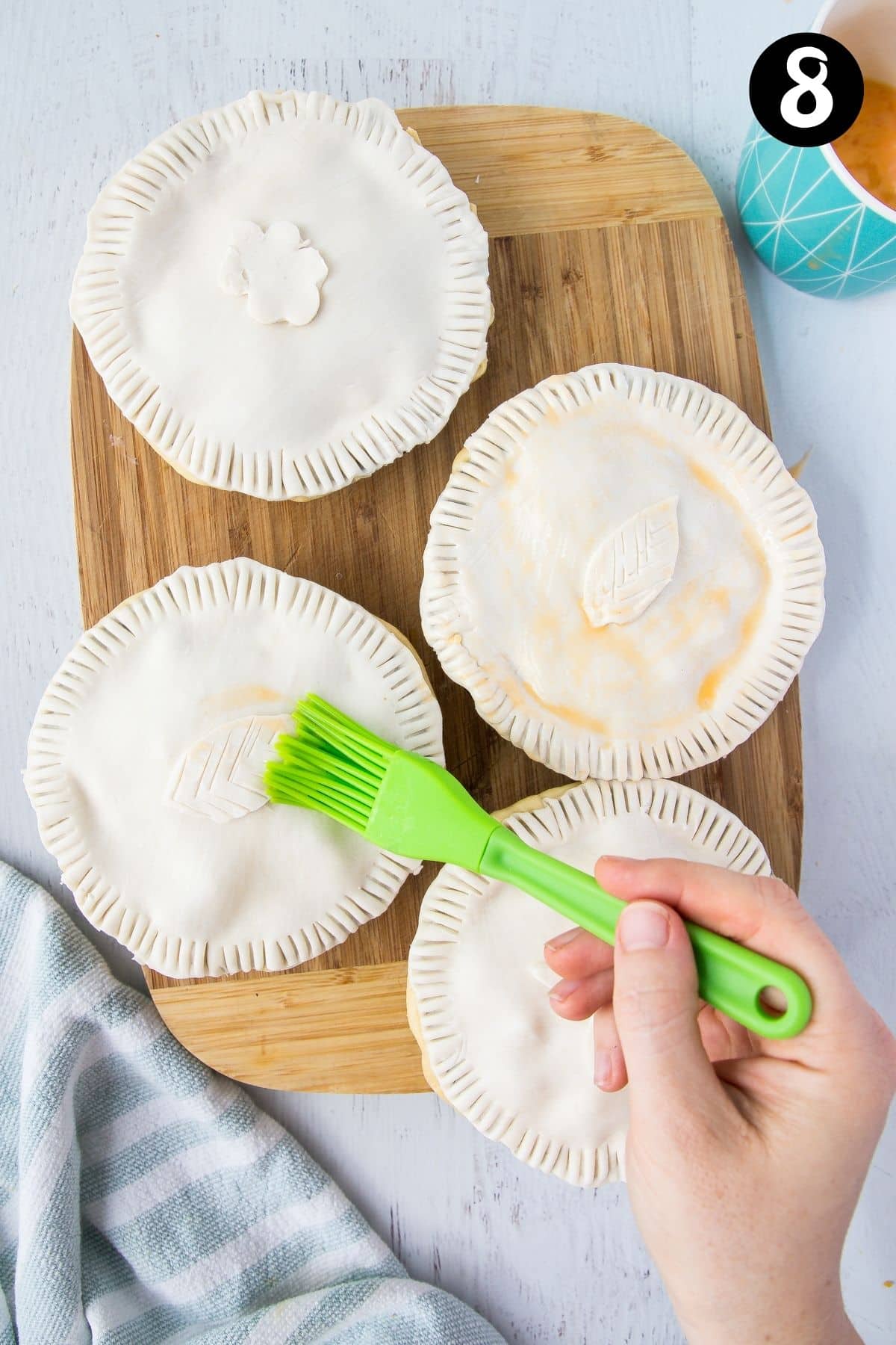 a hand brushing egg wash over uncooked pies