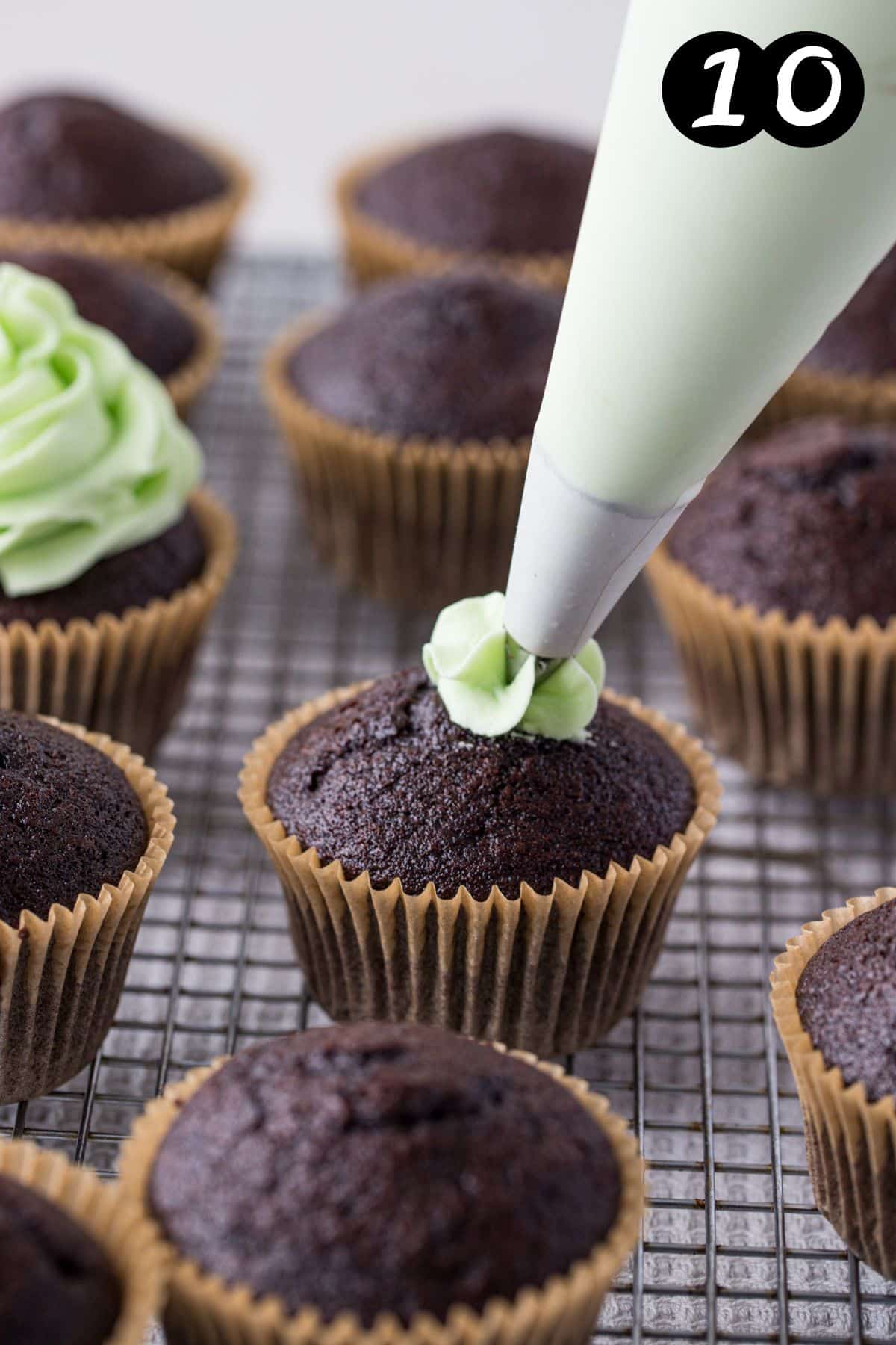 a piping bag piping mint buttercream onto a cupcake.