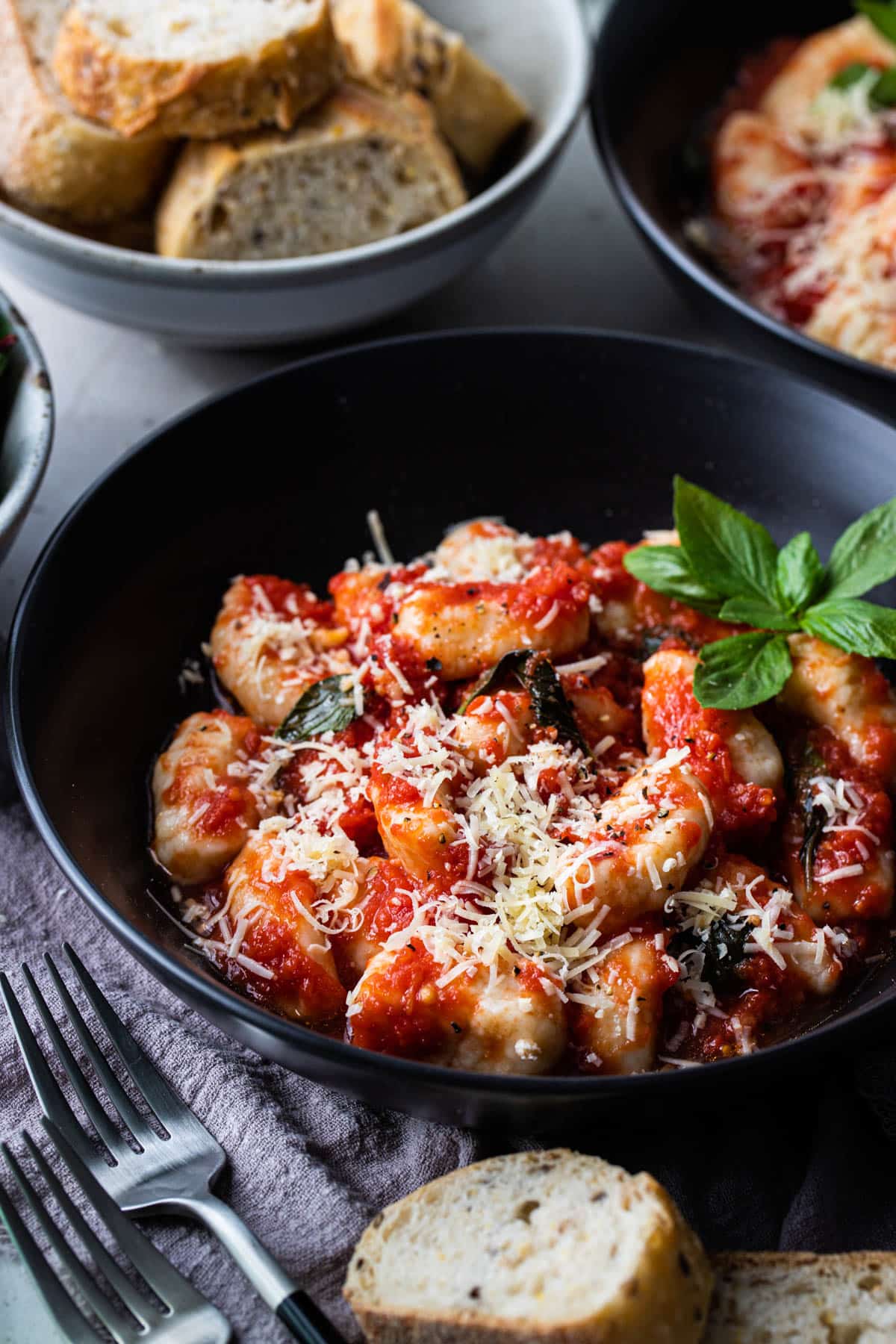 a black bowl with ricotta gnocchi topped with parmesan cheese and basil leaves.