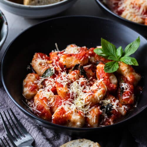 a bowl of ricotta gnocchi topped with cheese and basil.