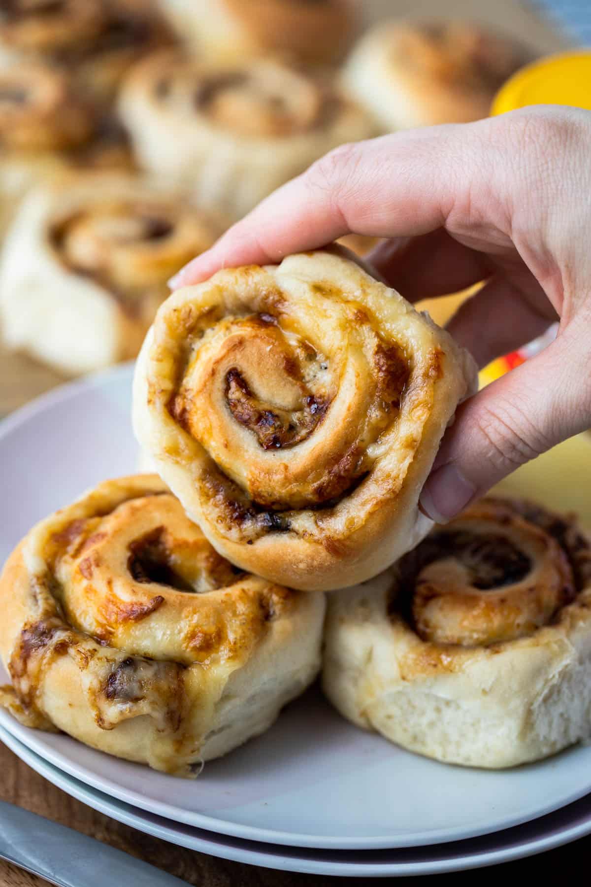 a hand holding a cheesymite scroll above a plate of scrolls.