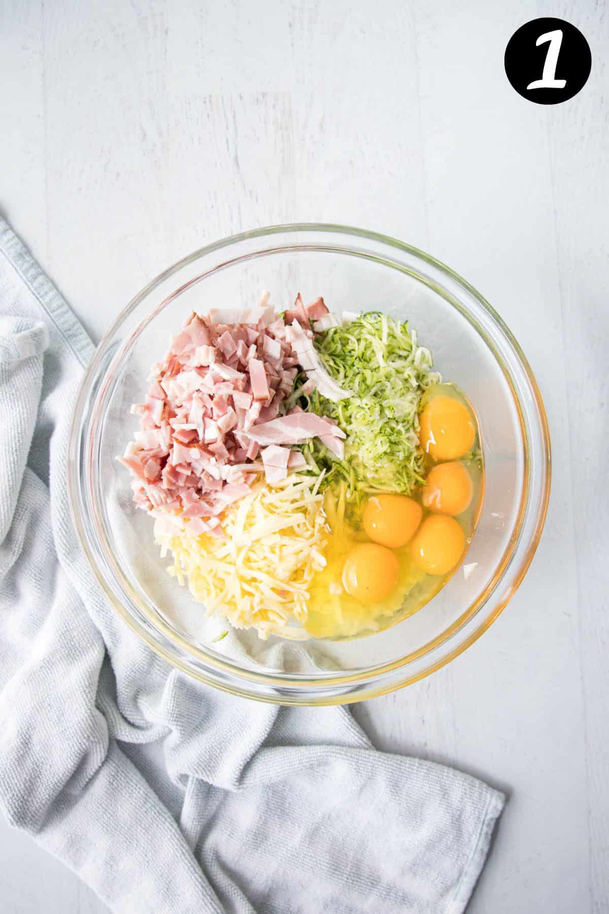 grated zucchini, bacon and eggs in a bowl with other ingredients.