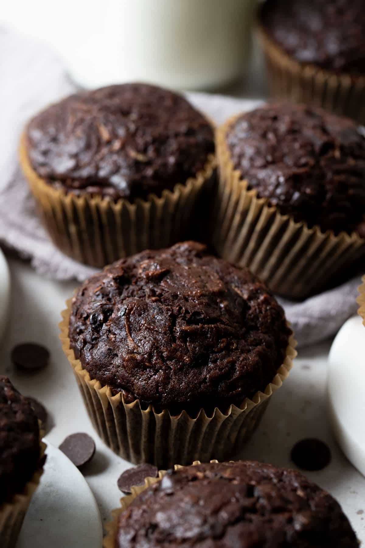 chocolate muffins in paper cases, arranged on a white table with chocolate chips.