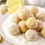 lemon bliss balls on a white plate with coconut and lemon slices.
