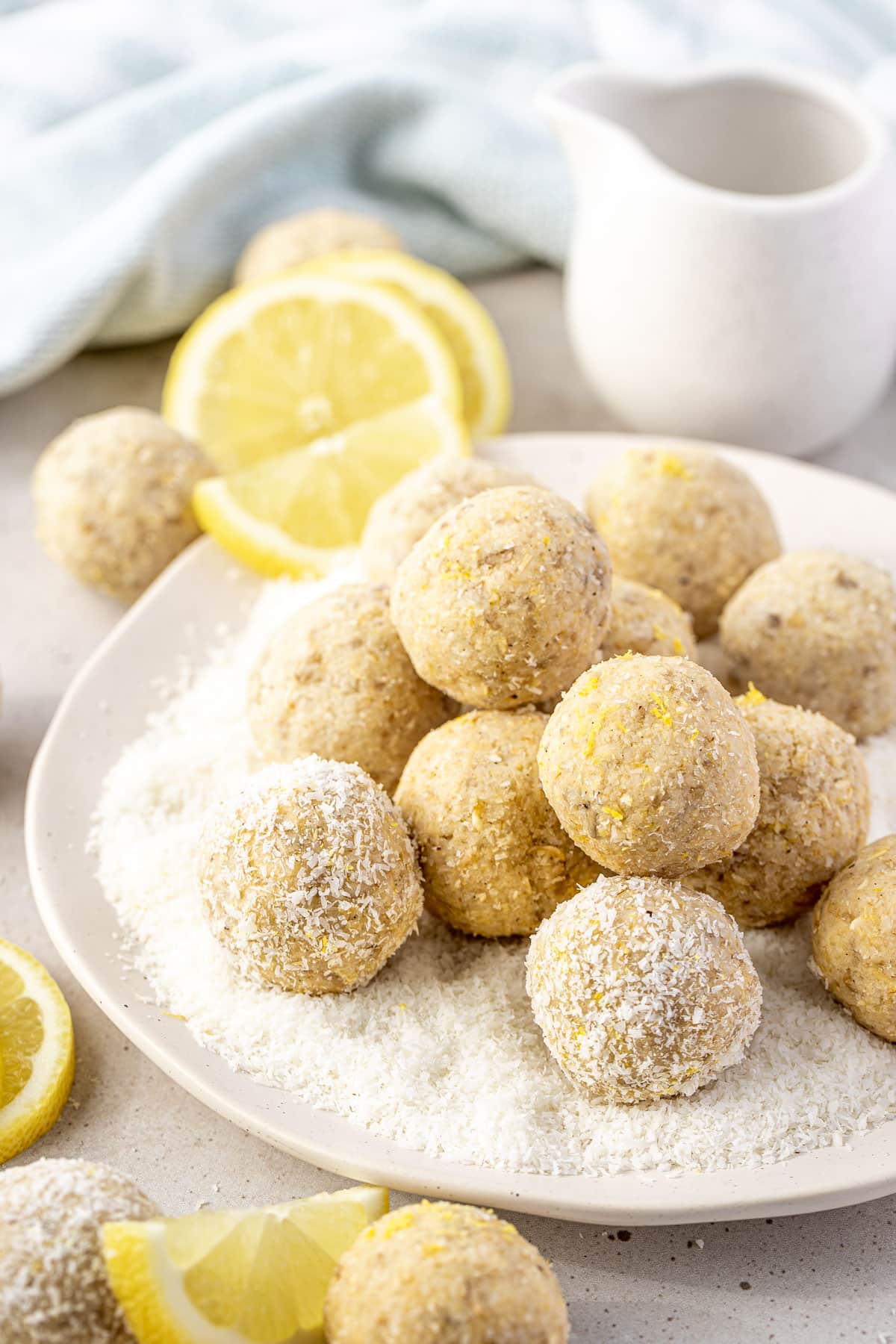 lemon bliss balls on a white plate with coconut and lemon slices.